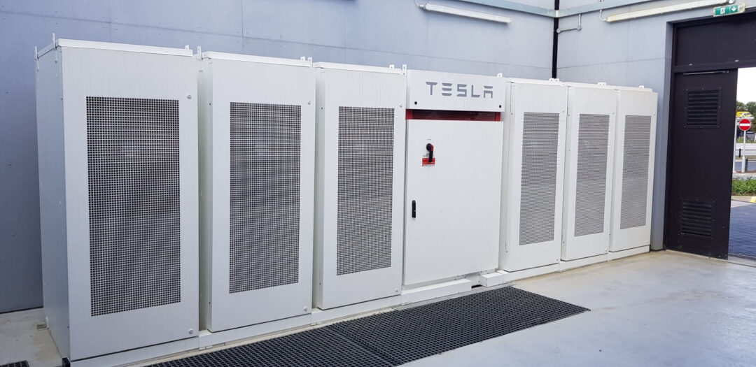 Tesla industrial battery storage units installed indoors, featuring multiple white enclosures lined side by side.