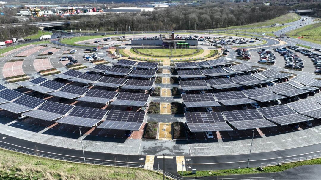 Large circular car park covered with multiple rows of solar carports, with vehicles parked beneath and road infrastructure surrounding the site.