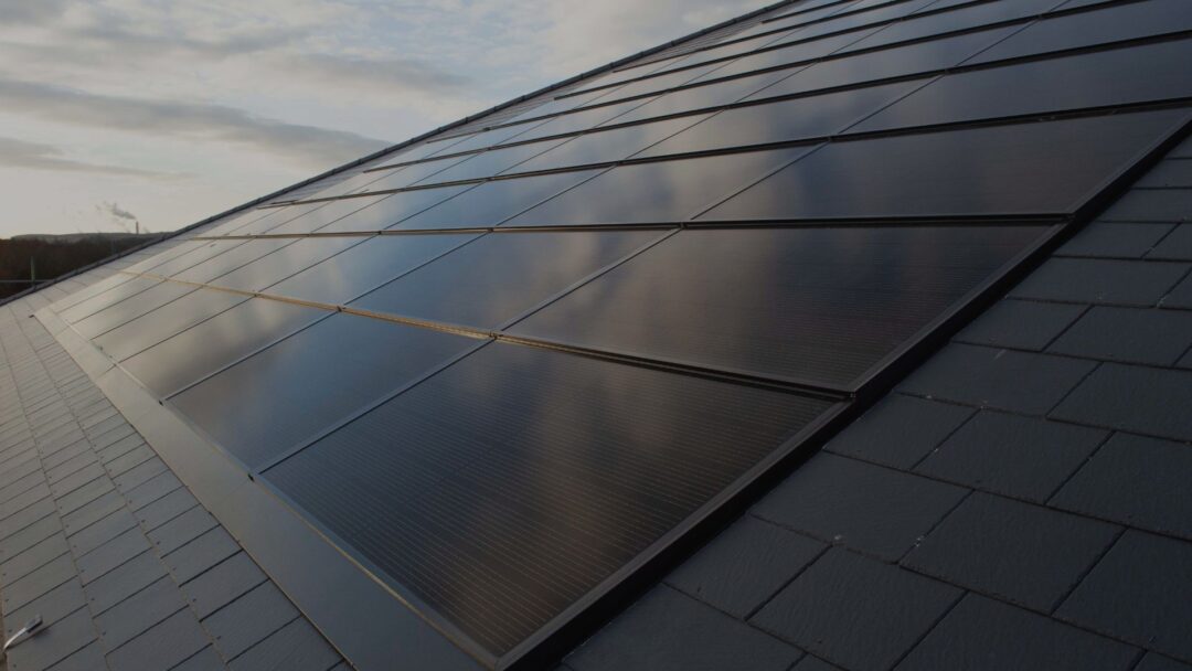Solar panels installed on a sloped tiled roof at sunset.