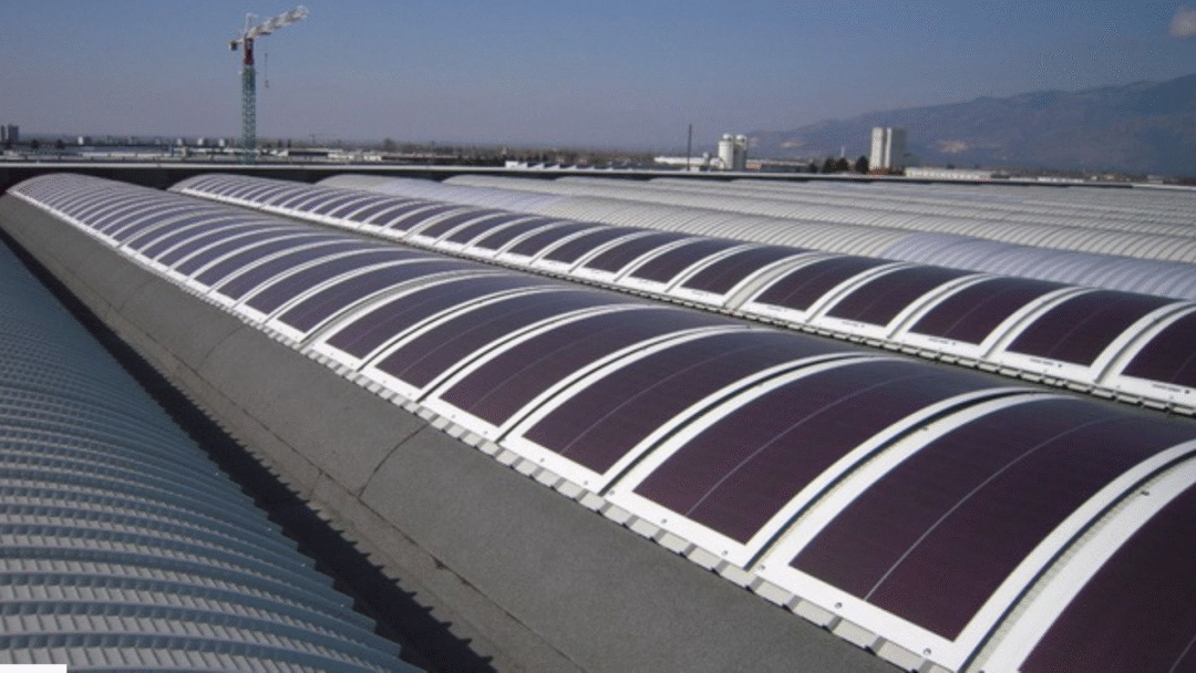 Curved industrial rooftop fitted with flexible solar panels in parallel rows.