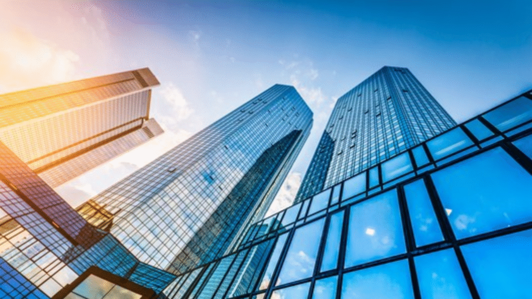 Upward view of modern glass skyscrapers reflecting sunlight against a bright blue sky.