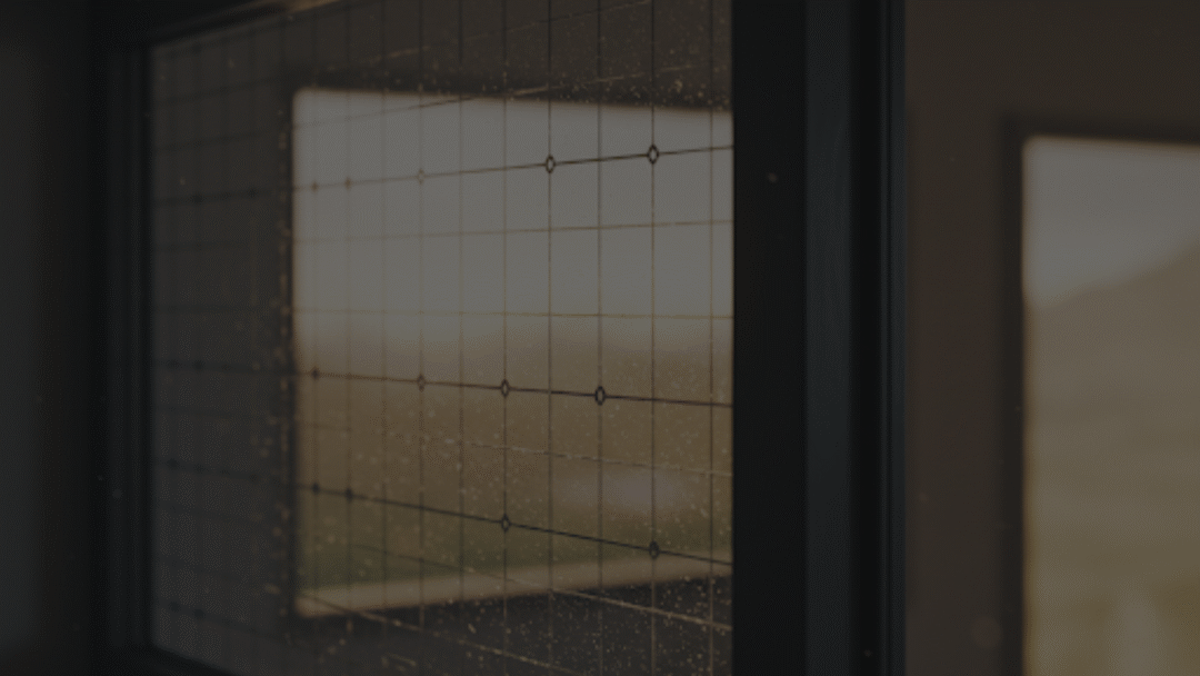 Close-up of a semi-transparent solar window panel with a subtle grid of photovoltaic cells, looking out onto a softly blurred outdoor landscape.