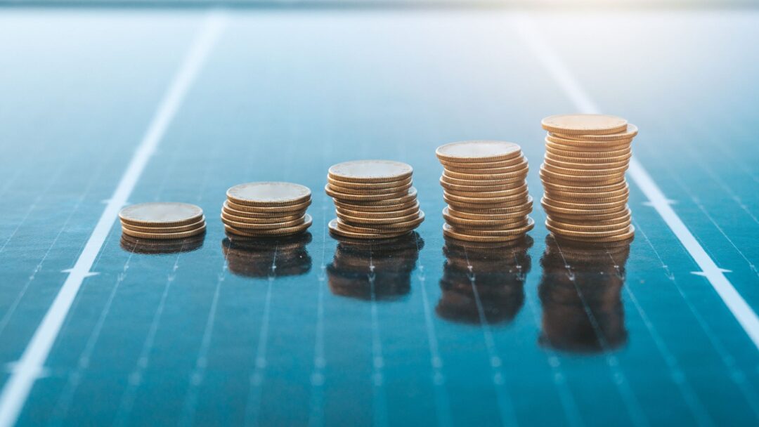 Increasing stacks of gold coins placed on a solar panel, symbolizing financial savings, investment, and profitable returns from renewable energy in Lease to Own