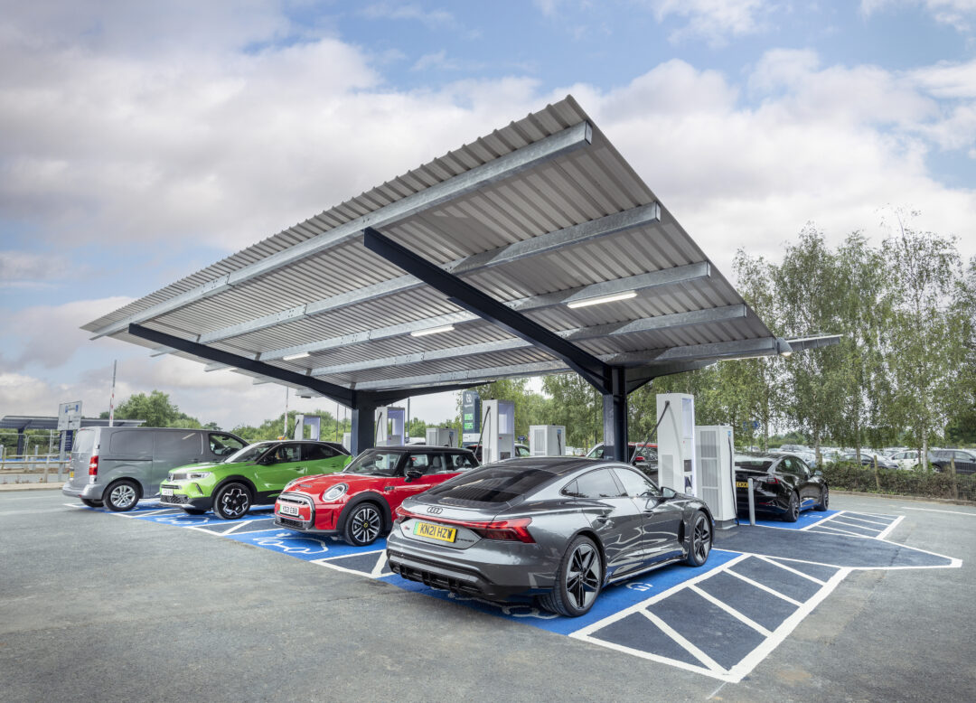 Covered electric vehicle (EV) charging station canopy with multiple fast charging units and bays, featuring various modern electric cars in our ESG Report