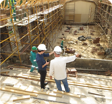 Construction workers and site managers in hard hats inspecting a building under renovation with scaffolding in place on Aerospace