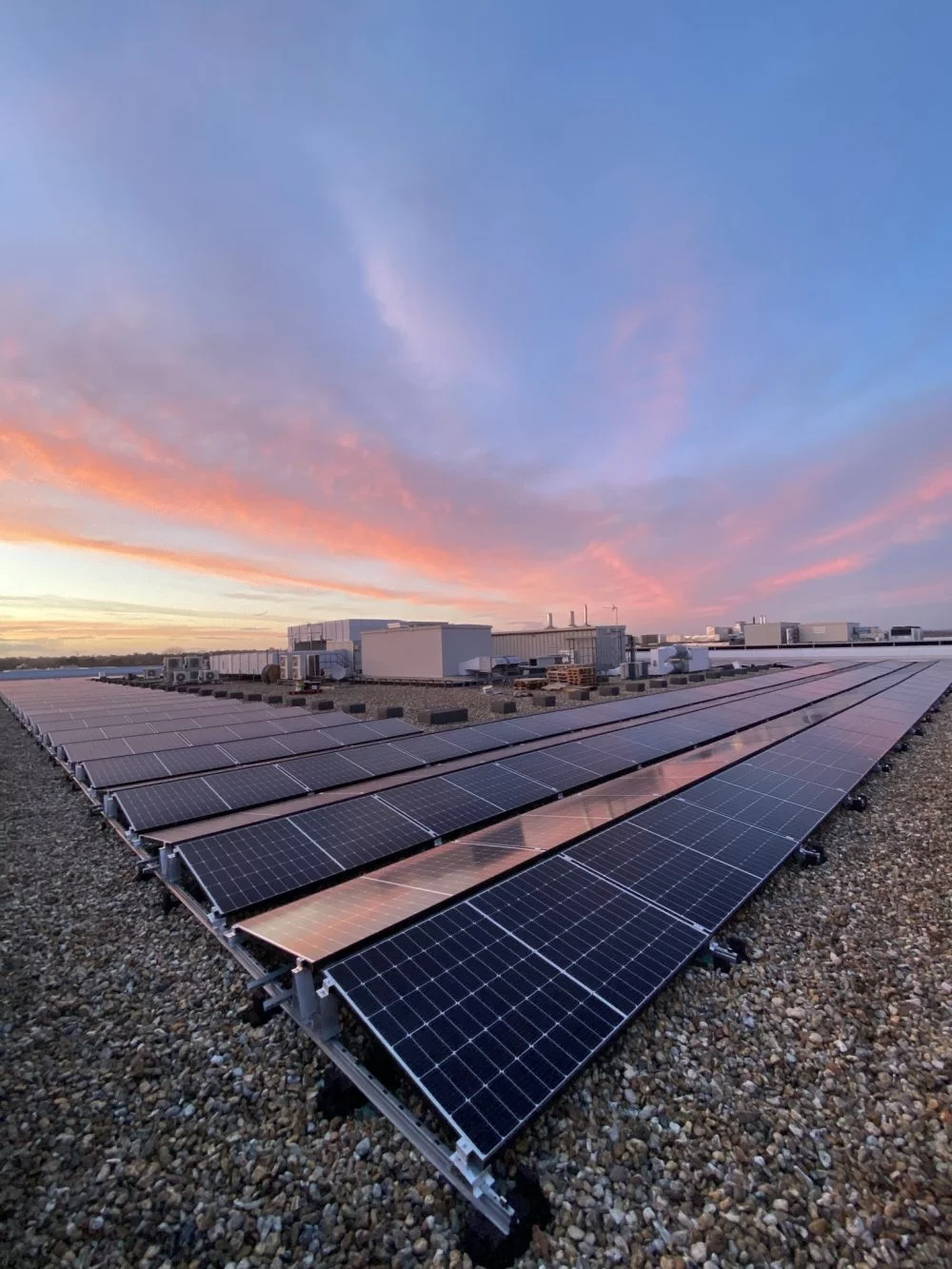 Rooftop solar panel array on a commercial building at sunrise with a colorful sky in the background in Aerospace