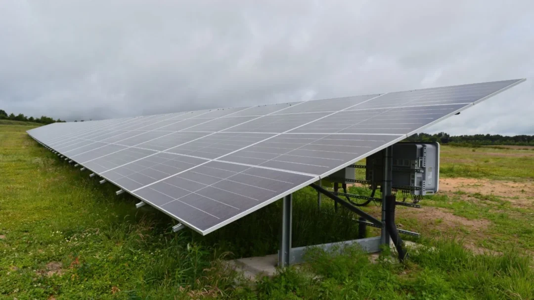 Close-up view of a ground-mounted solar panel array installed on metal supports in a grassy field under an overcast sky.