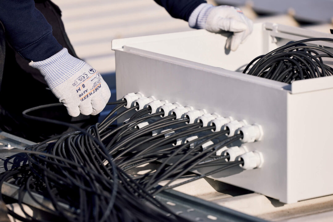 An engineer organizing and connecting multiple solar cables inside a rooftop junction box during a commercial PV installation.
