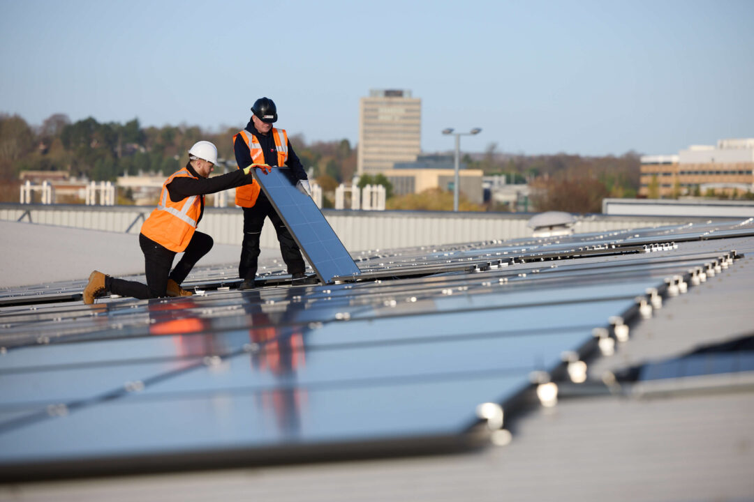 Two engineers installing a solar panel on a large commercial rooftop solar array, ensuring precise alignment for optimal system performance
