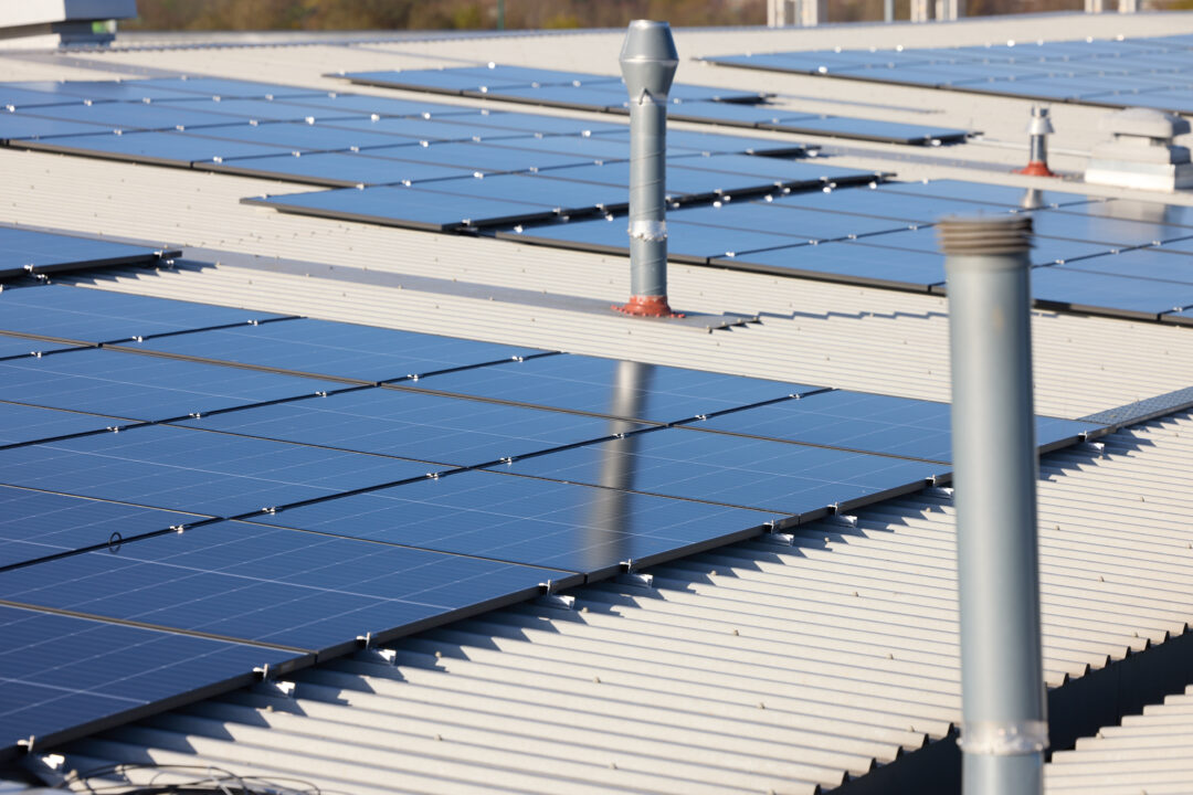 Rows of solar panels installed on a large commercial metal rooftop with ventilation ducts visible in the background.