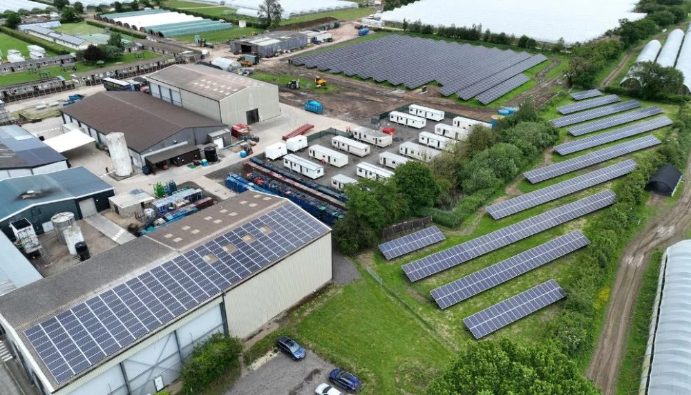 Aerial view of a commercial site with rooftop and ground-mounted solar panels across industrial buildings and farmland in Services.