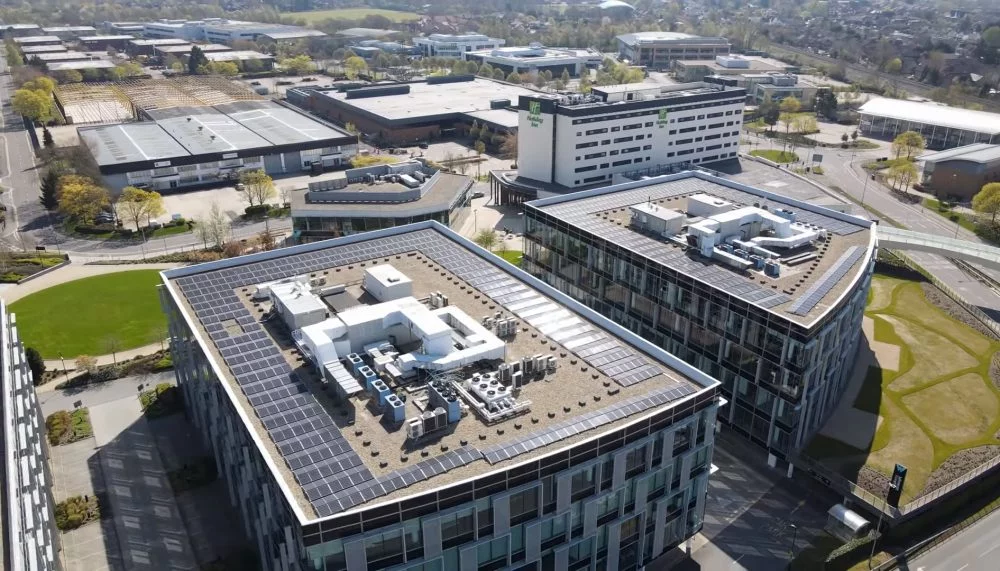 Aerial view of commercial office buildings with rooftop solar panels installed across large flat roofs in a modern business park.