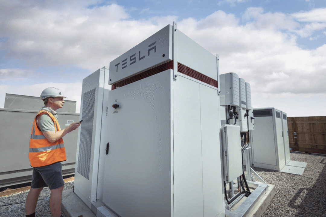Engineer inspecting Tesla battery storage systems at a commercial energy site, showcasing renewable energy infrastructure.