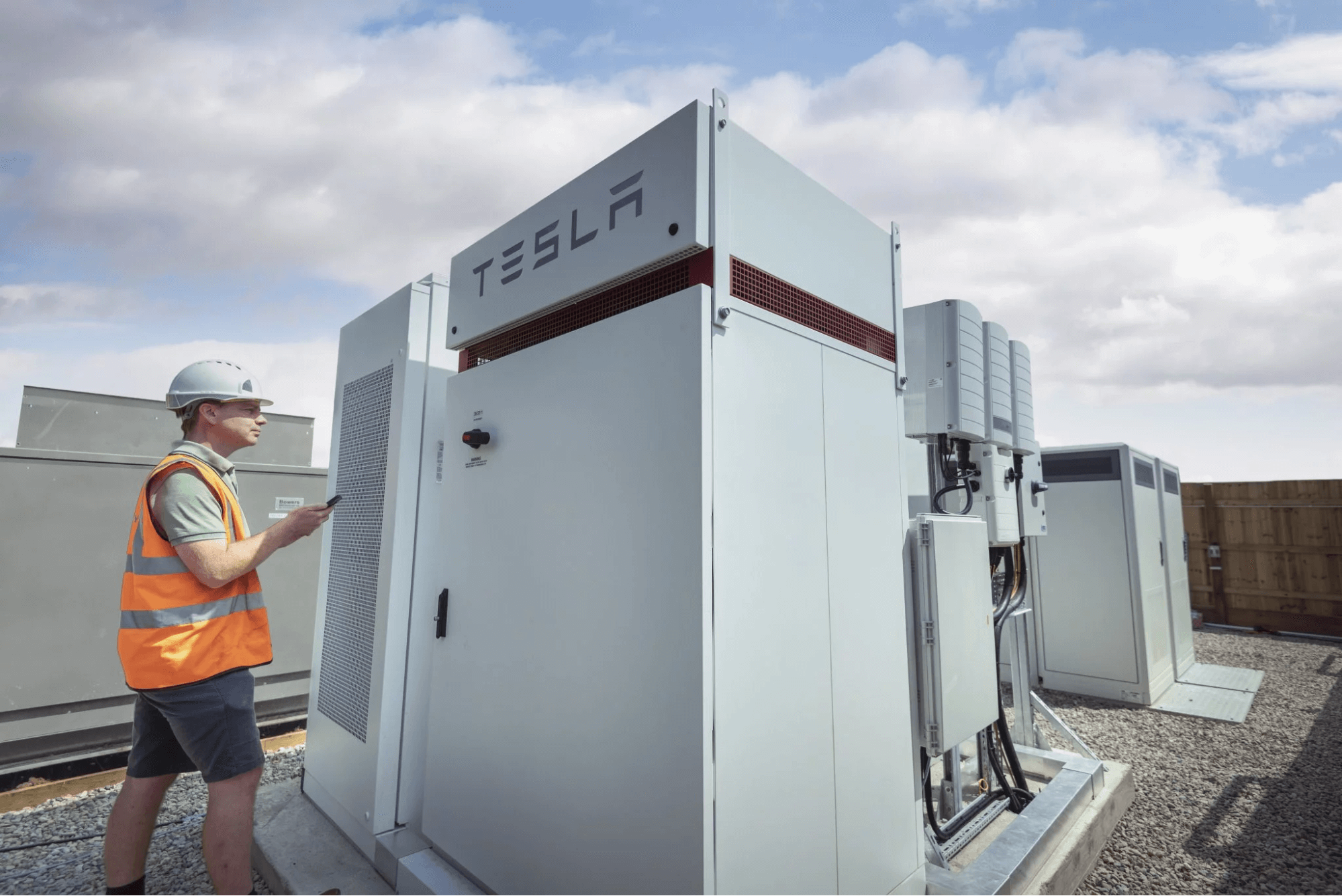 Engineer inspecting Tesla battery storage systems at a commercial energy site, showcasing renewable energy infrastructure.