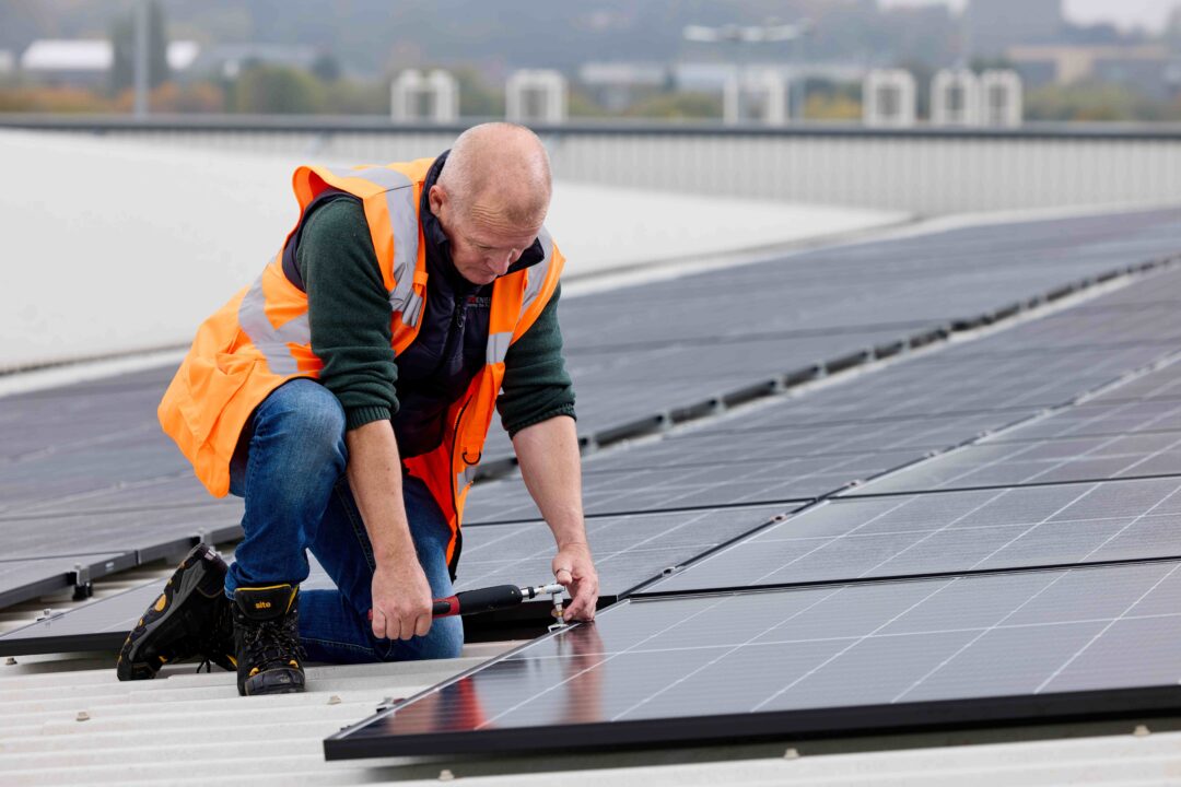 Solar installer in a high-visibility vest securing rooftop solar panels during a commercial PV installation.