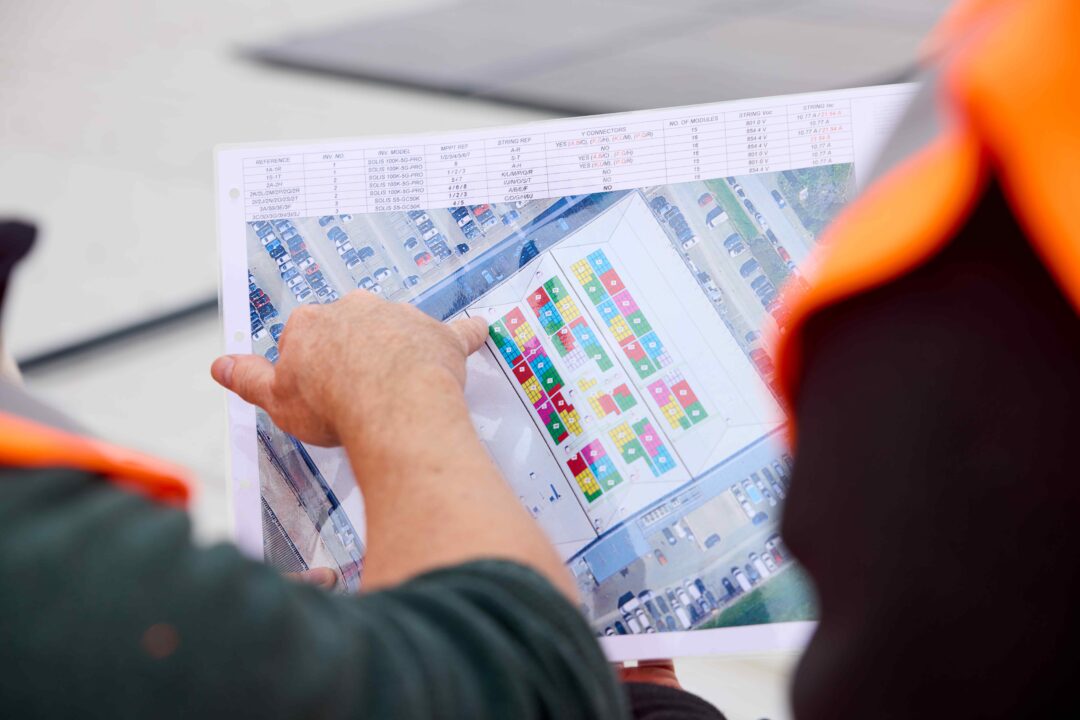 Engineers reviewing a rooftop solar panel layout plan, pointing at a colour-coded site map during a commercial solar installation project.