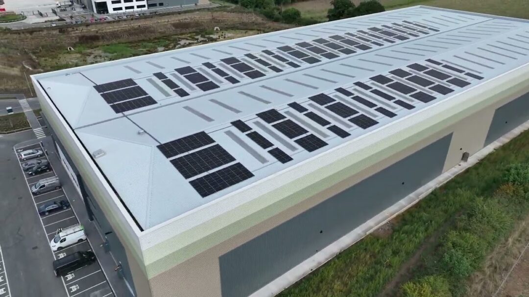 Heavy-duty expanded metal mesh security cage or enclosure under a corrugated canopy, located next to a facility parking lot and landscaped area in Furniture Box