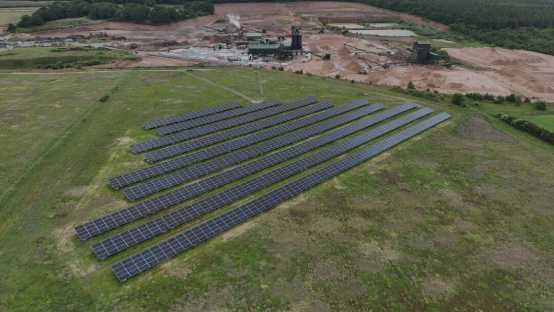 Aerial view of a ground-mounted solar panel array installed on a grassy field near an industrial quarry site, generating renewable energy for commercial operations in Mansfield Sand.