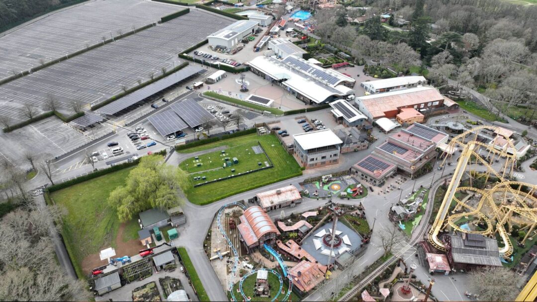 Aerial view of a theme park with solar panel installations on rooftops and carports, showcasing clean energy integration across rides, visitor centres, and parking facilities in Paultons Park.
