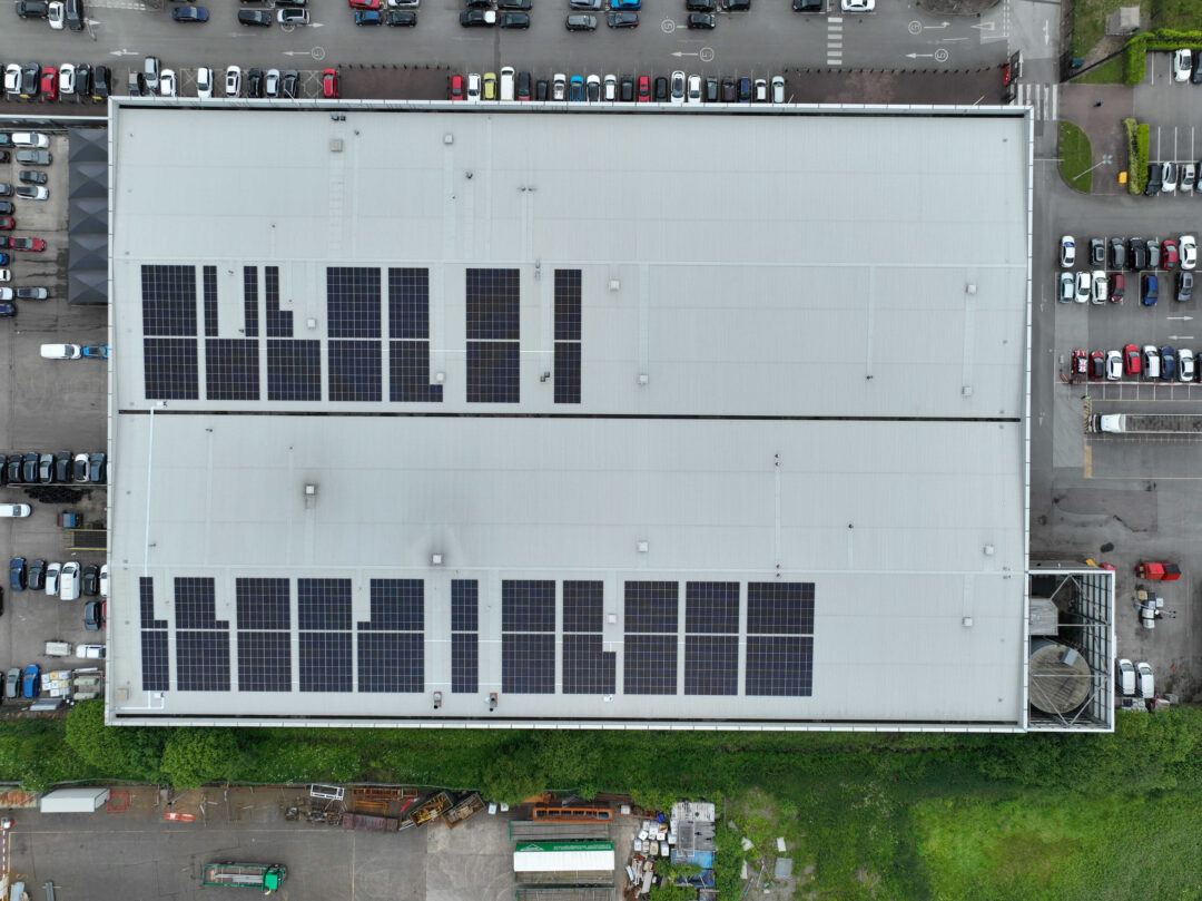 Top-down drone shot of Arnold Clark building displaying rooftop solar panel layout and surrounding infrastructure.