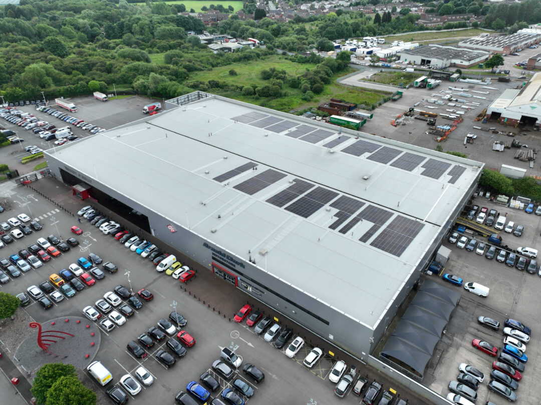 Aerial view of Arnold Clark’s large warehouse with solar panels installed on the roof, featuring a full car park and surrounding green space.
