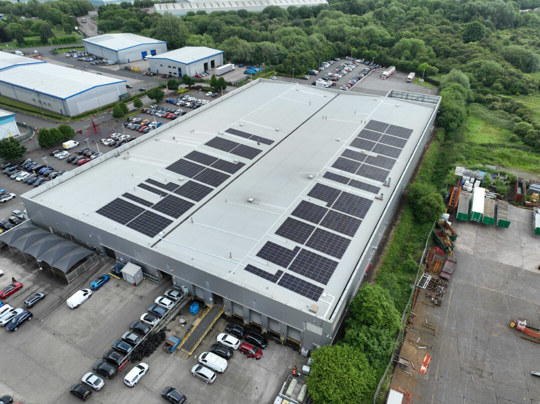 Rear aerial angle of Arnold Clark facility showcasing solar PV panels across the full rooftop with adjacent loading bays and industrial units.