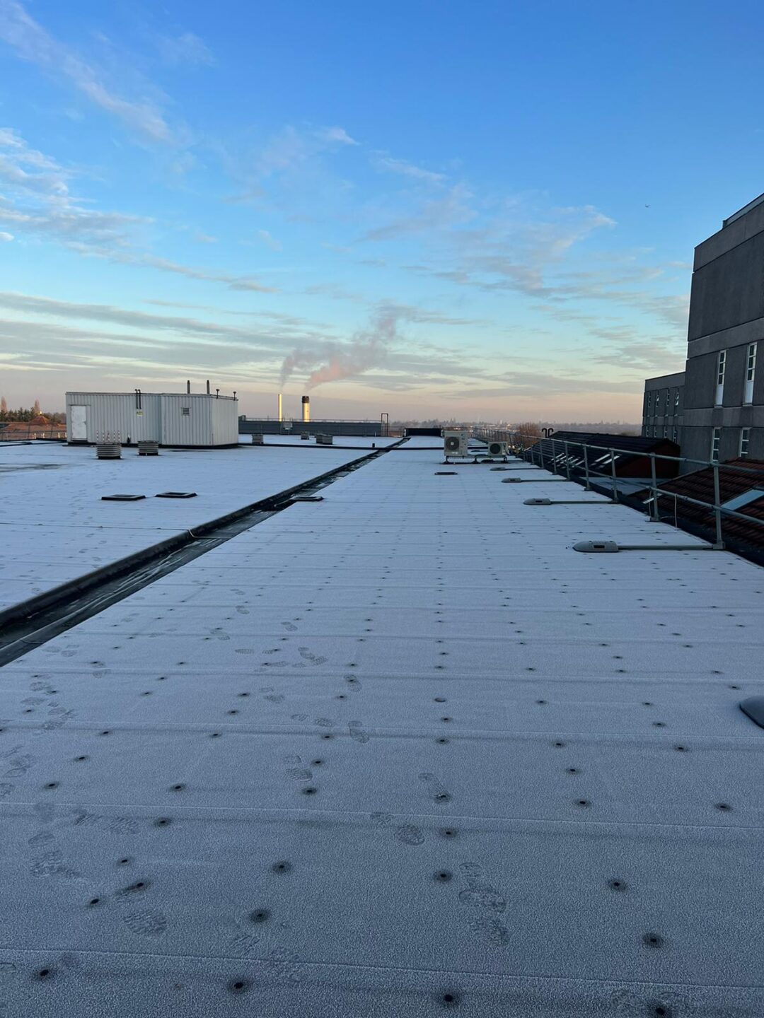 Frost-covered rooftop at Heartland Hospital prior to solar panel installation, with visible footprints and morning sky in the background.