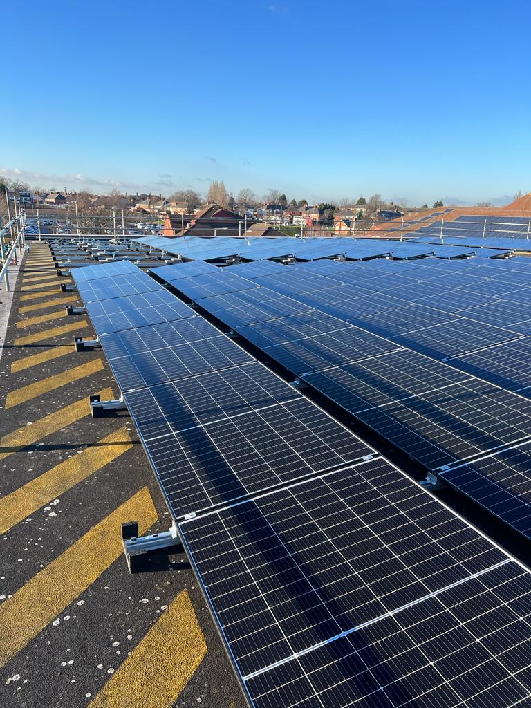 Solar panels installed on the Heartland Hospital rooftop on a clear day, with yellow safety markings and distant buildings in the background.