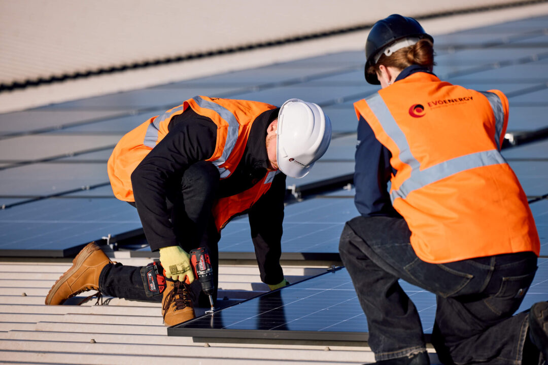EvoEnergy engineers installing solar panels on a commercial rooftop, securing photovoltaic modules during solar PV installation.